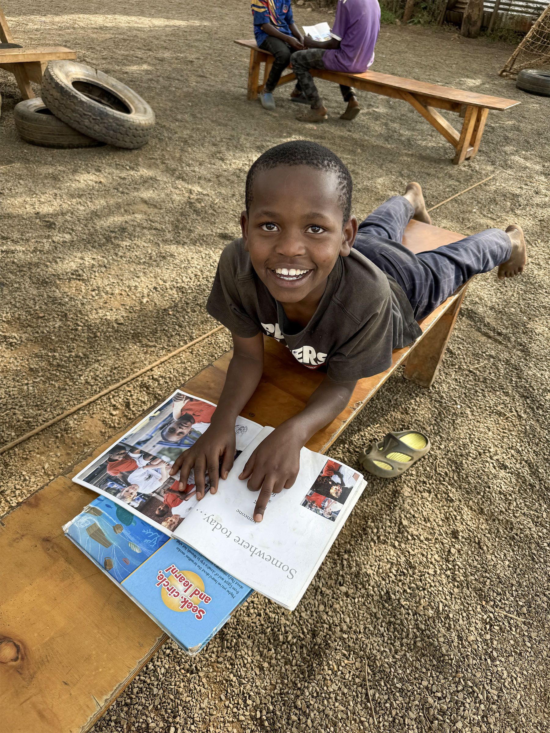 A smiling boy reading a book outdoors at Embrace Centre Nairobi