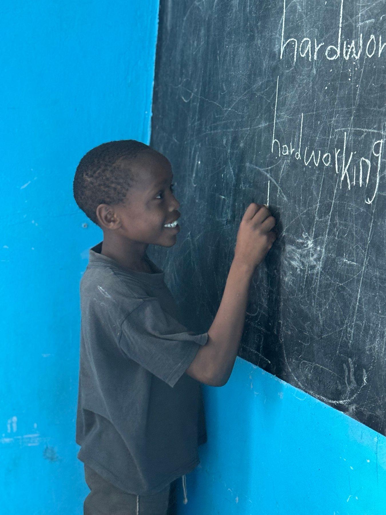 A boy writing on a chalkboard during academic support at the Embrace Centre